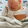 baby, sleeping, blanket, pillow, dinosaur_print, infant, cozy, white_clothing, closeup, child, soft_fabric, peaceful, cute, indoors, portrait, head, face, skin, resting, nap