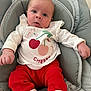 baby, infant, child, cute, clothing, red_pants, white_shirt, cherry_graphic, cushion, seat, indoor, portrait, small_hands, wide_eyes, expression, cozy, striped_pattern, soft_fabric, sitting, young