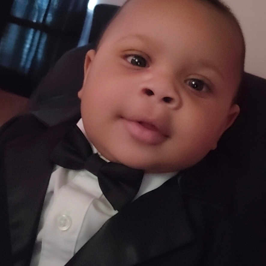 Malik is registered to the contest to win money with this photo: baby, tuxedo, bow_tie, formal_wear, child, portrait, indoor, face, cute, infant, black_jacket, white_shirt, smile, young_child, person, head, curly_hair, eyes, fashion, baby_boy