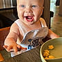 Stetson joined the competition — help win amazing prizes! baby, child, high_chair, food, snack, table, bowl, indoor, smiling, happy, blue_eyes, clothing, person, restaurant, wood, light, face, cute, reaching, dining