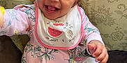 Zuri is registered to the contest to win money with this photo: baby, child, smile, happy, sitting, couch, clothing, bib, white_pants, pink_top, footwear, sock, face, hand, indoor, person, cute, infant, portrait, joyful