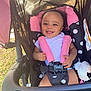 baby, smiling, stroller, child, infant, seatbelt, toy, plush, outdoor, sunlight, happy, white_clothing, pink, black, polka_dot, person, cute, seat, baby_toy, portrait