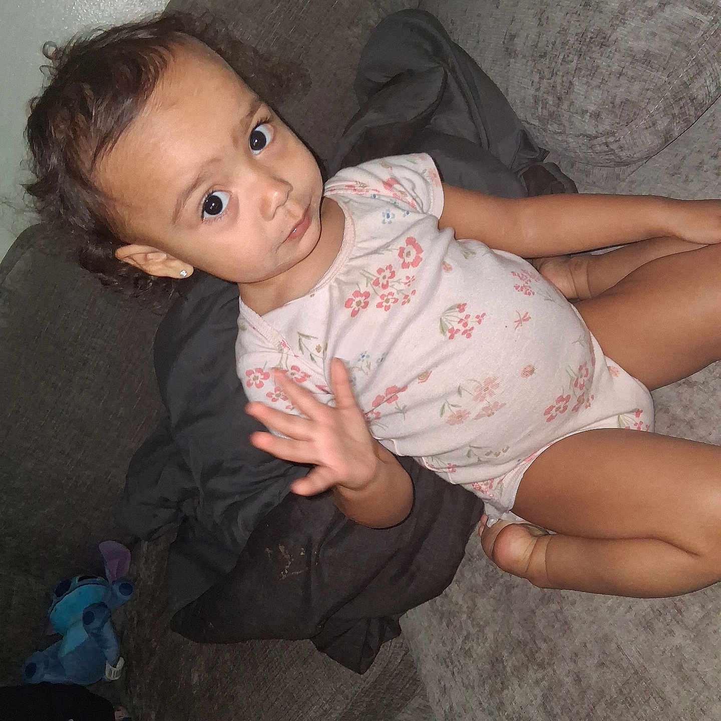 Dariely'S is registered to the contest to win money with this photo: casual_clothing, child, couch, cozy, curly_hair, earrings, expression, face, furniture, home, indoor, onesie, person, plush_toy, relaxing, smile, sofa, toddler, wave, young_child