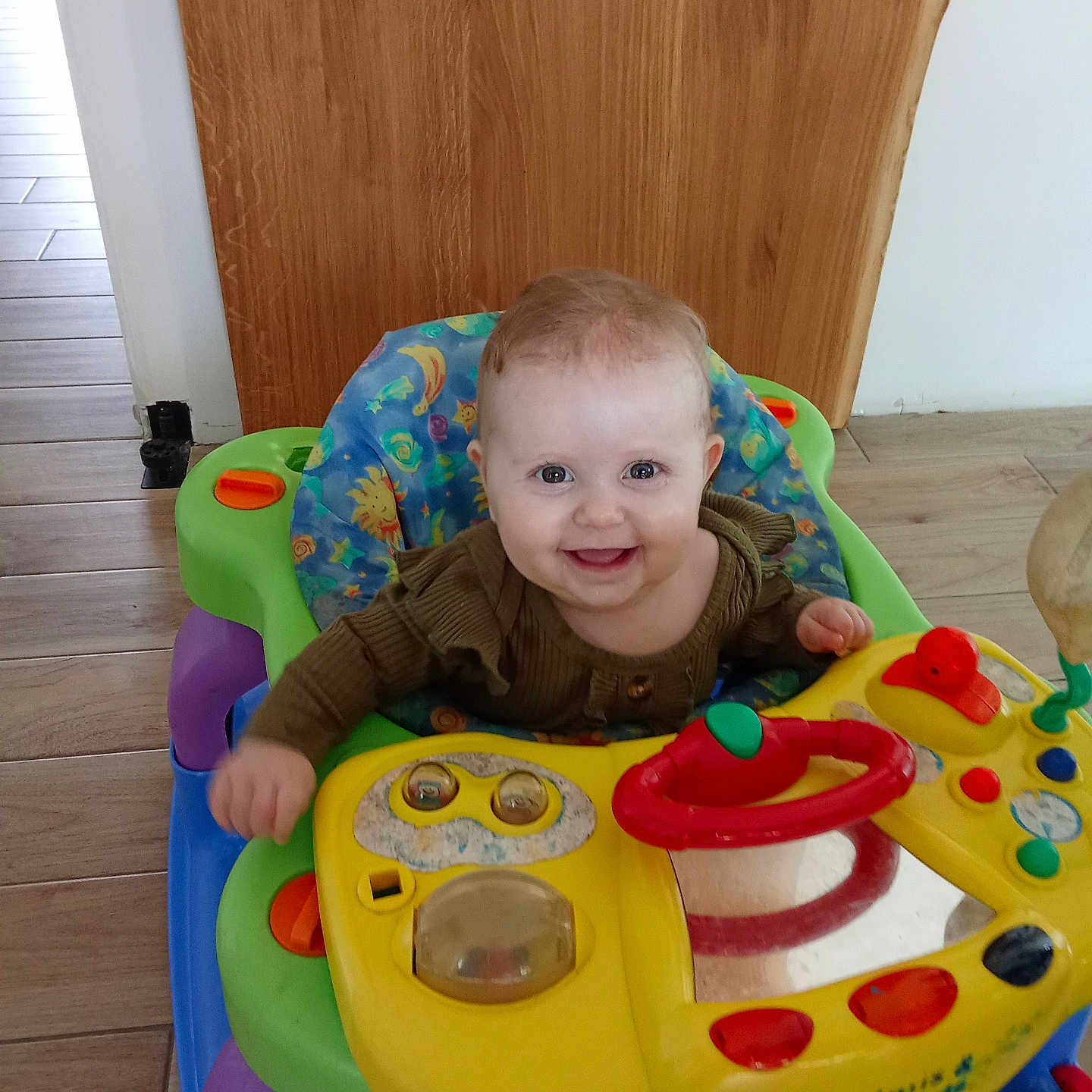 Jenny participe au concours pour gagner de l'argent avec cette photo : baby, child, clothing, colorful, cute, expression, face, floor, happy, indoor, infant, person, play, seat, smile, toy, walker, wooden_floor, wooden_wall, young