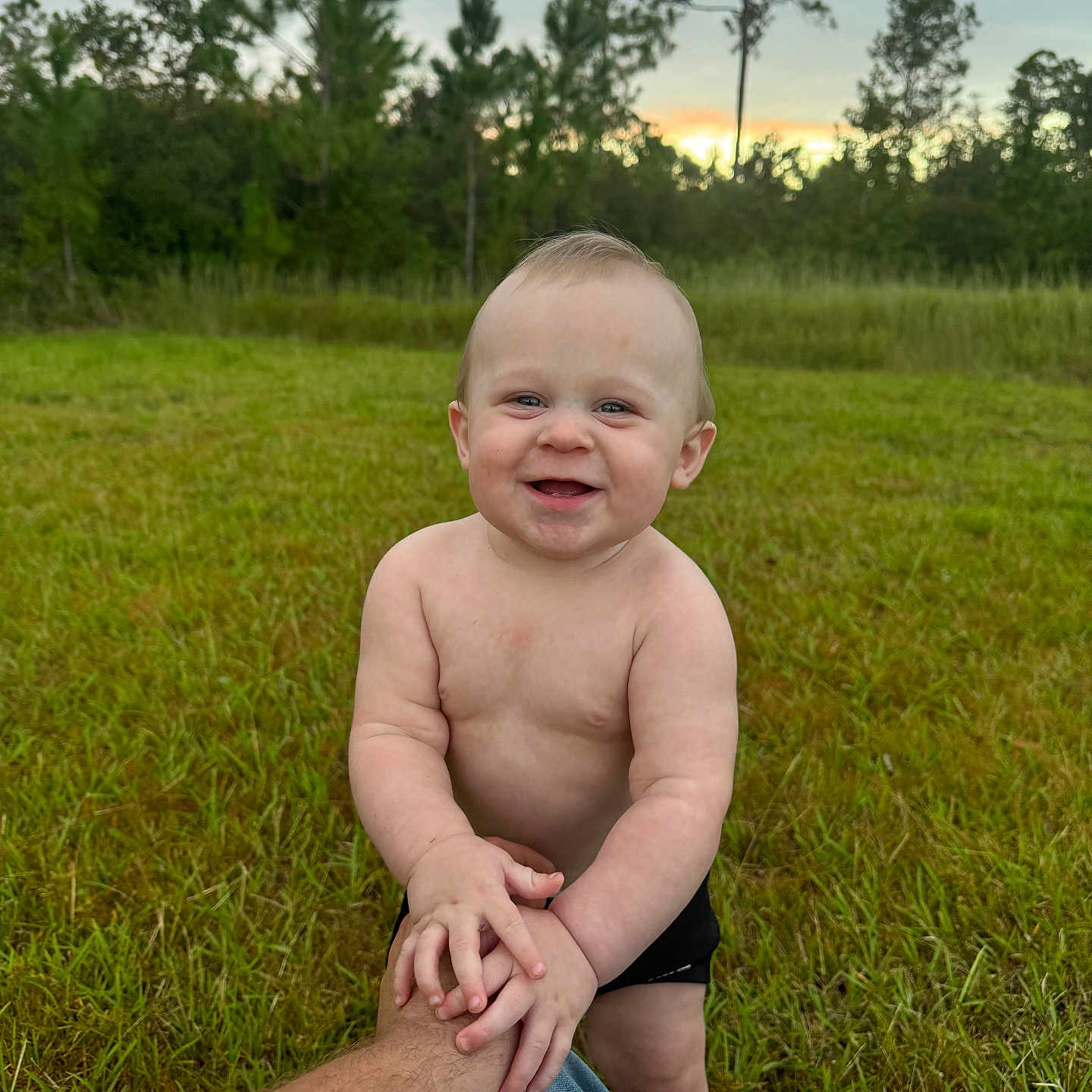 Michael is registered to the contest to win money with this photo: baby, bodypart, clothing, face, finger, grass, hand, happy, head, pants, person, photography, plant, portrait, shorts, sitting, skin, smile, tattoo, tree