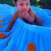 Kadel is registered to the contest to win money with this photo: baby, blue, child, citrus, curly_hair, cute, eating, fence, fruit, garden, inflatable_pool, orange, outdoor, pool, portrait, sitting, snack, summer, sunlight, toddler
