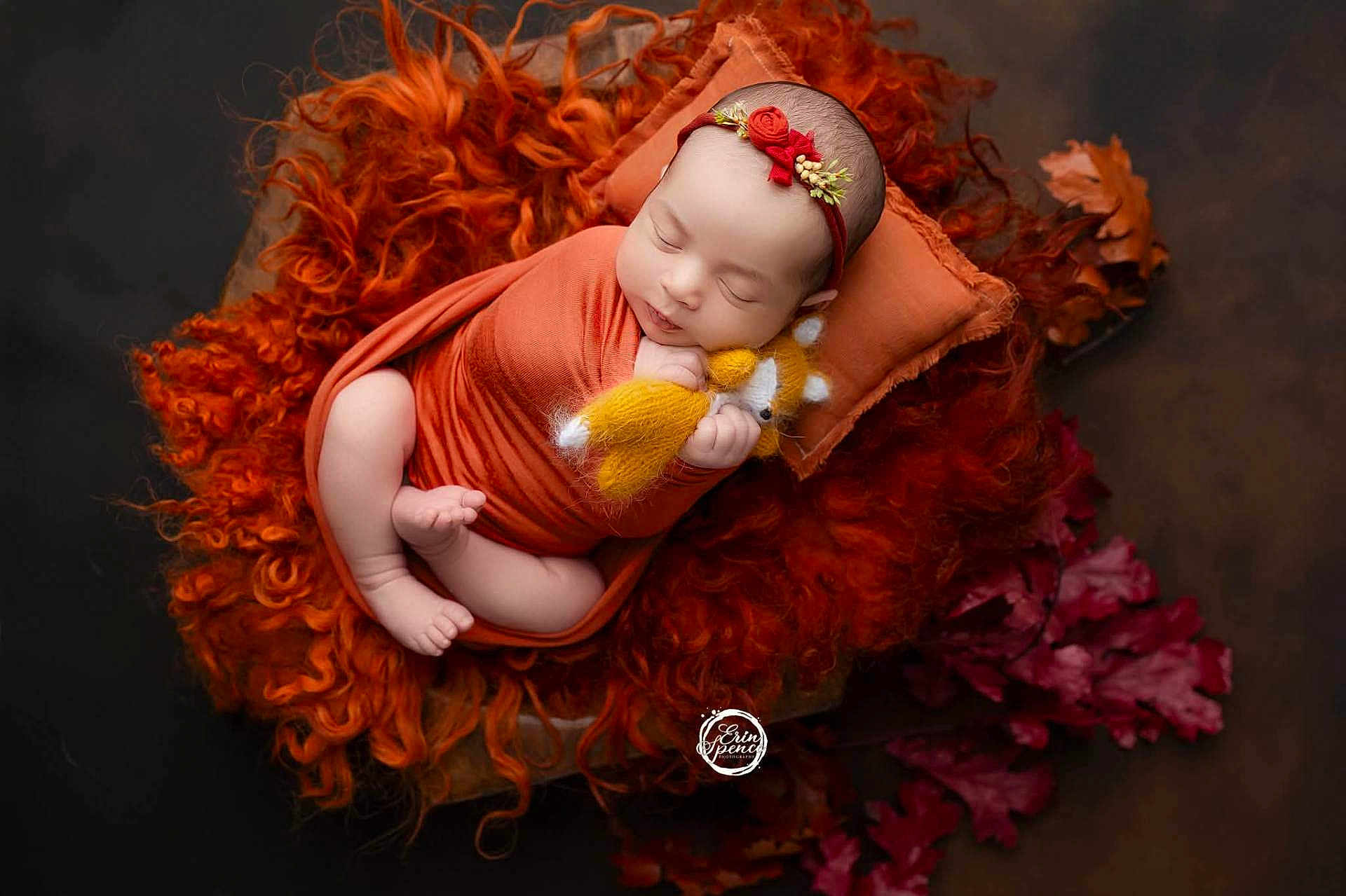 Ember joined the competition — help win amazing prizes! baby, newborn, swaddled, orange_wrap, pillow, blanket, stuffed_toy, yellow_fox, sleeping, headband, flower_headband, curly_blanket, autumn_leaves, soft_lighting, portrait, infant, peaceful, cozy, indoor, cute