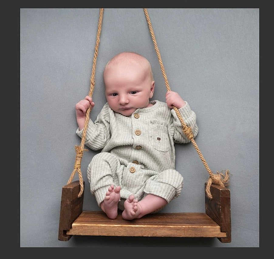 Vinnie is registered to the contest to win money with this photo: baby, infant, swing, wooden_swing, ropes, pajamas, cozy, striped_clothing, barefoot, gray_background, cute, child, portrait, indoor, newborn, seated, hands, feet, wood, baby_clothes