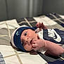 baby, newborn, infant, hat, clothing, nike, onesie, bed, bedspread, pattern, face, hand, skin, lying_down, indoors, cute, small, person, portrait, sleepwear