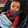 baby, infant, stroller, blanket, red_clothing, striped_clothing, face, person, indoor, seat_belt, knitted_blanket, curious_expression, blue_blanket, child, baby_girl, baby_boy, sitting, close_up, head, cute