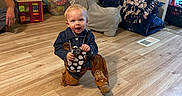 Whyatt is registered to the contest to win money with this photo: baby, child, toddler, cowboy_costume, denim_jacket, hat, boots, toy_phone, smiling, indoor, playroom, wood_floor, toys, blankets, cushions, furniture, portrait, sitting, crouching, home