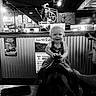 baby, child, toddler, smiling, bow_tie, mechanical_bull, ride, indoor, sports_bar, restaurant, black_and_white, portrait, seated, happy, blond_hair, face, furniture, brick_wall, signs, entertainment