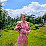 Millie is registered to the contest to win money with this photo: woman, baby, child, outdoor, grass, trees, sky, clouds, smiling, holding, red_checkered_clothing, tattoos, nature, sunny, happy, portrait, dress, person, greenery, summer