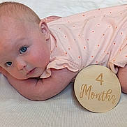 Millie is registered to the contest to win money with this photo: baby, infant, 4_months, lying_down, polka_dot, peach_outfit, wooden_sign, curious_gaze, soft_surface, cute, child, portrait, skin, blue_eyes, resting, newborn, young_baby, indoors, sleepwear, close_up
