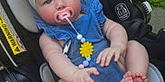 Millie is registered to the contest to win money with this photo: baby, infant, pacifier, headband, bow, car_seat, blue_outfit, outdoor, grass, safety_warning, child, cute, pink, yellow_flower, beads, feet, hands, summer, daylight, portrait