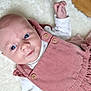baby, blue_eyes, child, clothing, corduroy, cute, face, floor, hand, indoors, infant, lying_down, pink_dress, portrait, skin, smiling, soft_texture, white_blanket, wooden_buttons, young