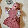 baby, card, celebration, child, clothing, cute, happy, illustration, indoors, infant, lying_down, one_month, person, pinafore, pink_dress, portrait, small_fist, smiling, white_rug, wooden_floor