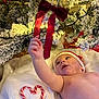 baby, santa_hat, christmas_tree, red_bow, candy_cane, heart_shape, blanket, holiday, festive, lights, decoration, snow_flocked_tree, infant, reaching_hand, indoors, cute, celebration, christmas, soft_texture, child