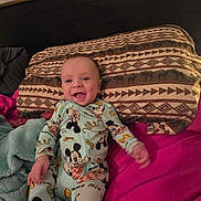 Toby joined the competition — help win amazing prizes! baby, infant, mickey_mouse, pajamas, smile, pillow, blanket, bed, pink_sheet, headboard, curtain, pattern, happy, portrait, lying_down, hand, feet, cute, indoors, linens