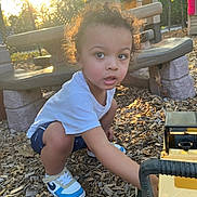 Kawhi joined the competition — help win amazing prizes! toddler, child, curly_hair, white_shirt, blue_shorts, sneakers, toy_truck, playground, wood_chips, sunset, outdoor, bench, picnic_table, fence, trees, daylight, person, crouching, curious, play