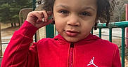 Kentrell joined the competition — help win amazing prizes! child, curly_hair, red_jacket, playground, outdoor, metal_bars, trees, bench, fence, sky, cloudy, person, face, expression, casual_clothing, young, portrait, daytime, nature, curious