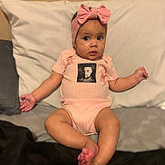 Legacie is registered to the contest to win money with this photo: baby, infant, child, pink_onesie, headband, bow, cute, sitting, bed, pillow, indoors, skin, feet, hands, expression, portrait, toddler, clothing, person, young_child