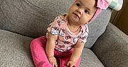 Legacie is registered to the contest to win money with this photo: baby, child, pink_bow, headband, hello_kitty, outfit, pink_pants, couch, gray_couch, blankets, stack_of_blankets, indoor, curious_look, seated, portrait, cute, infant, person, smiling, cozy