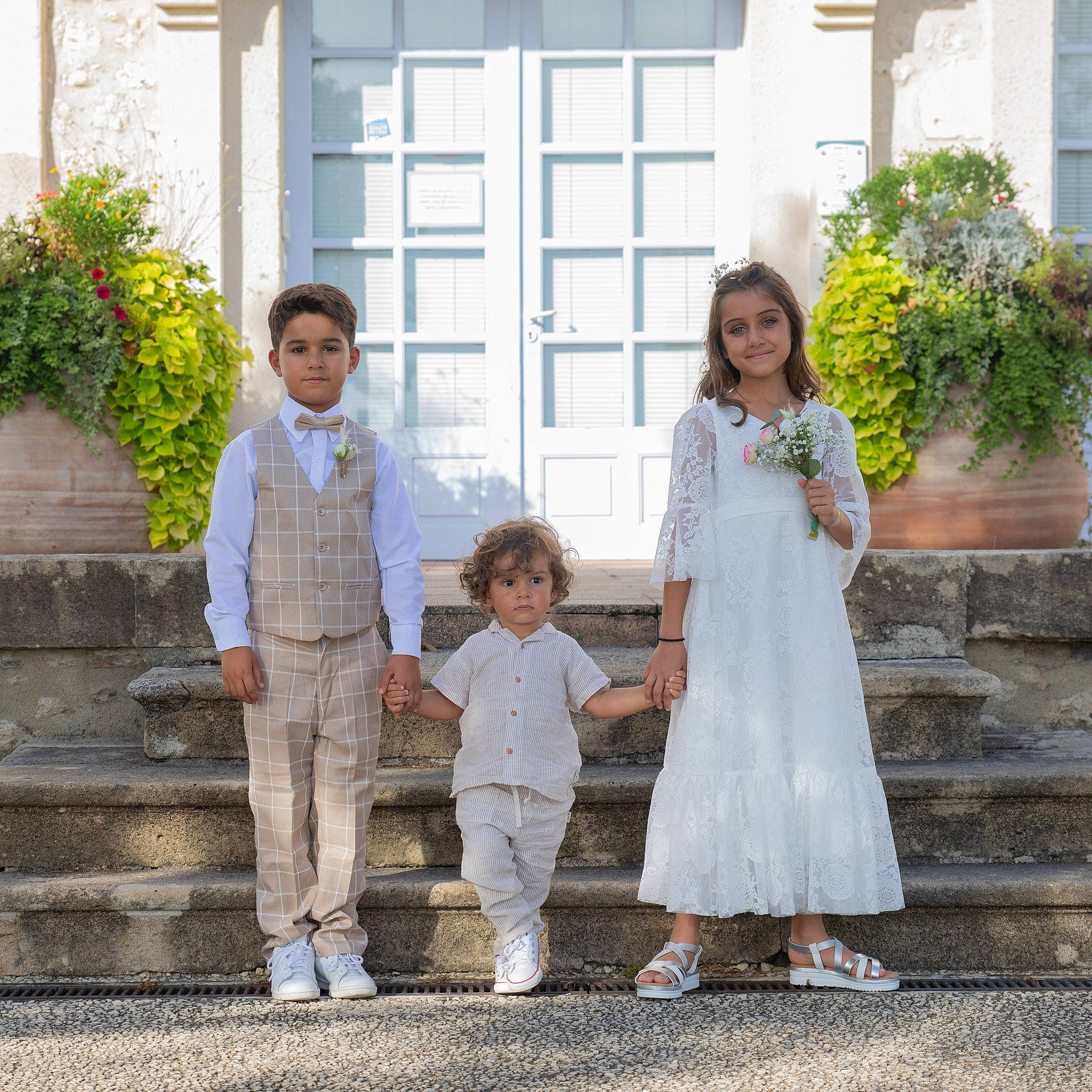 Lily-Rose participe au concours pour gagner de l'argent avec cette photo : bridal_clothing, bridal_party_dress, ceremony, child, dress, event, footwear, formal_wear, fun, gesture, happy, holding_hands, house, joy, leg, person, plant, sandal, toddler, waist