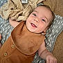 apparel, baby, bib, blanket, carpet, child, cloth, cute, fabric, face, hand, happy, indoors, infant, lying_down, person, portrait, skin, smiling, soft_toy
