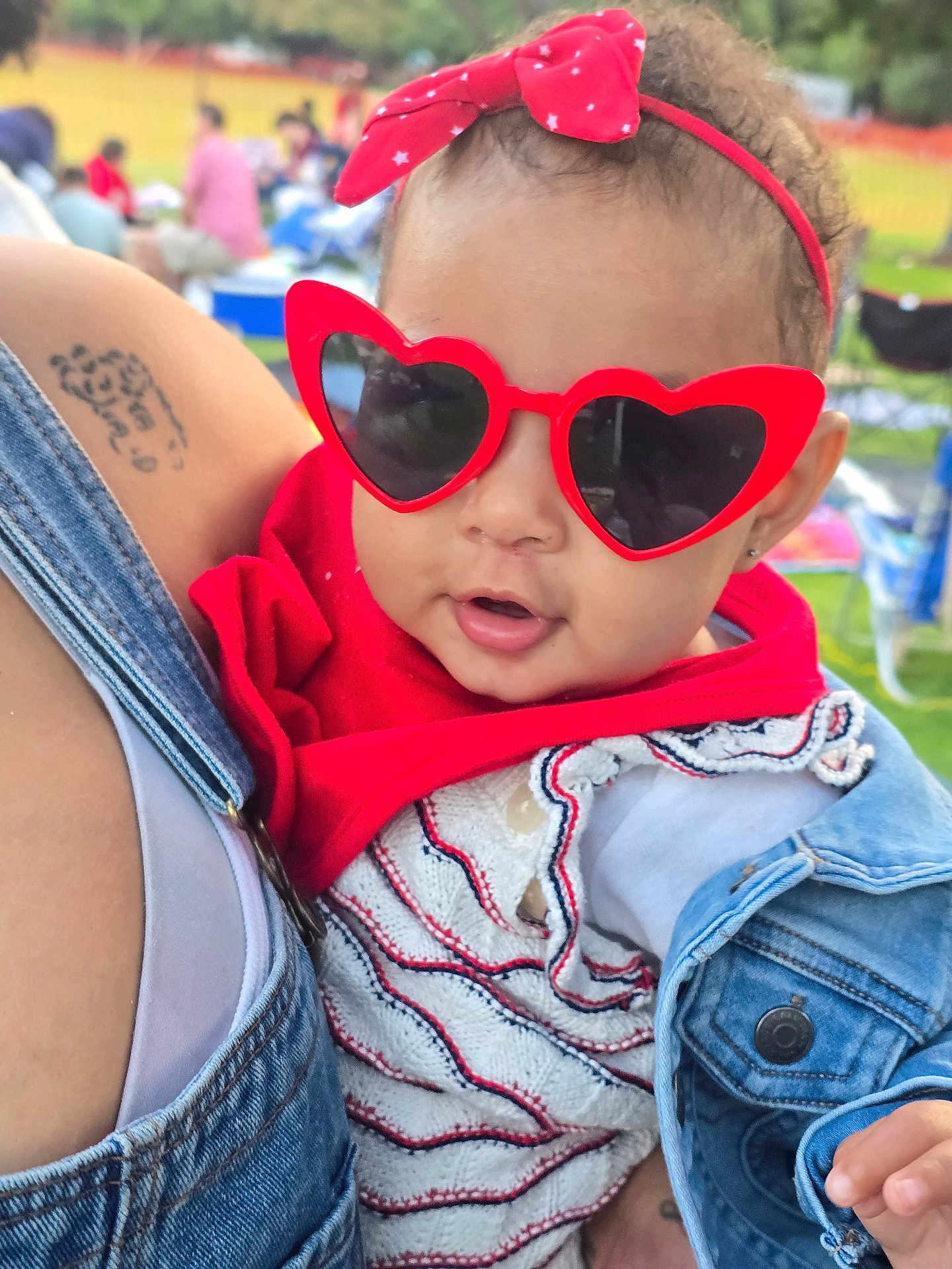 Amarís is registered to the contest to win money with this photo: accessory, baby, child, close_up, cute, denim_jacket, fashion, headband, heart_shaped, holding, infant, knitwear, outdoor, park, person, portrait, red, summer, sunglasses, tattoo