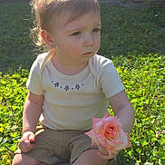 Dani is registered to the contest to win money with this photo: toddler, child, rose, flower, grass, outdoor, sunlight, greenery, shorts, shirt, earrings, nature, sitting, young_child, daylight, portrait, cute, serious, holding, plant