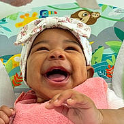 Paige is registered to the contest to win money with this photo: baby, smiling, headwrap, pink_towel, hand, happy, face, infant, closeup, cute, child, joy, colorful_background, animal_print, seated, portrait, skin, expression, playful, toddler