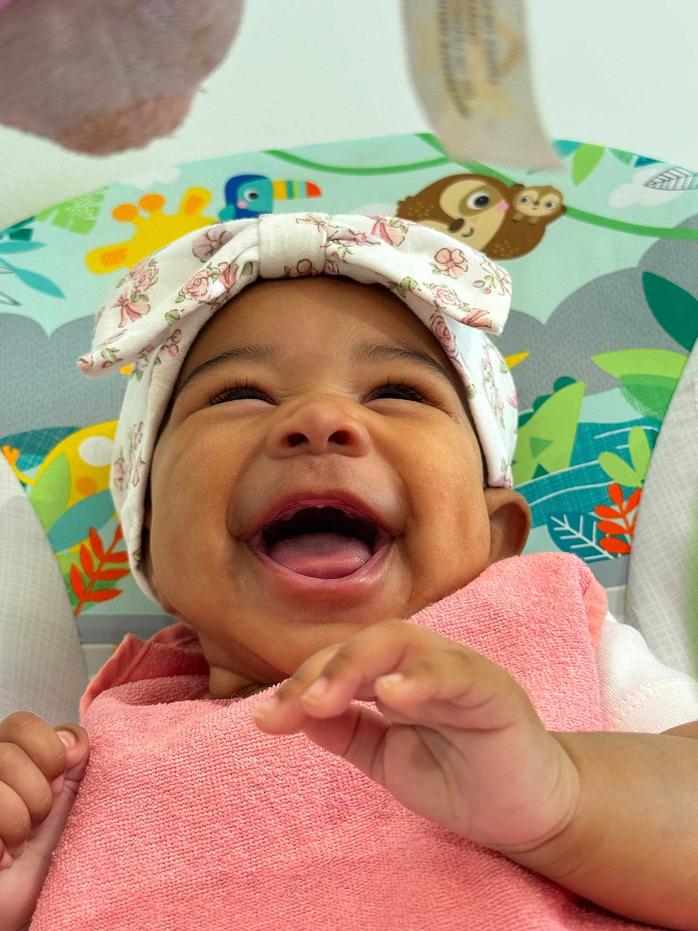 Paige is registered to the contest to win money with this photo: baby, smiling, headwrap, pink_towel, hand, happy, face, infant, closeup, cute, child, joy, colorful_background, animal_print, seated, portrait, skin, expression, playful, toddler