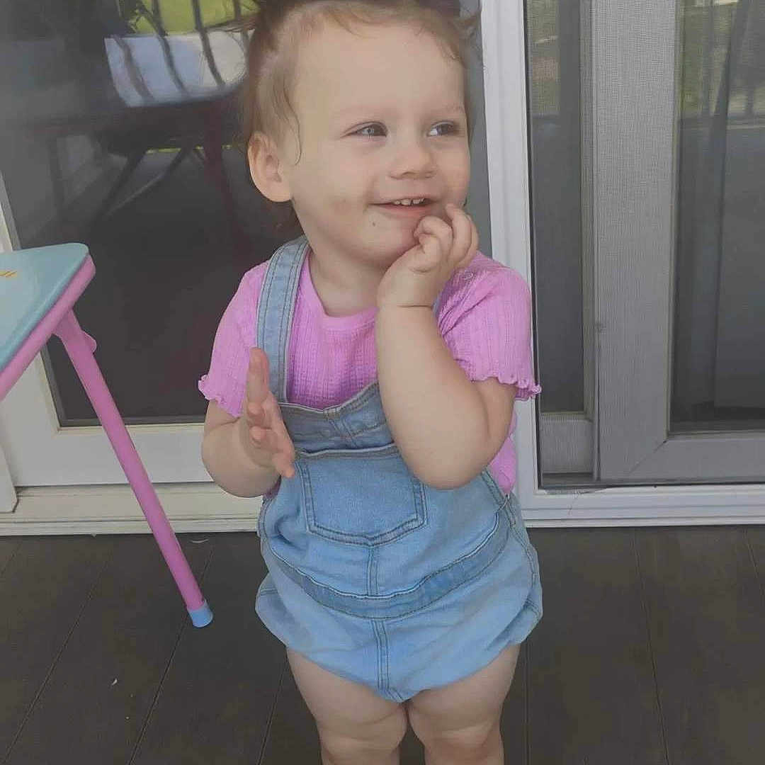 Malaya joined the competition — help win amazing prizes! toddler, child, pink_socks, denim_overalls, pink_shirt, standing, porch, wooden_floor, hair_buns, smiling, happy, outdoor, daylight, clapping, young_child, person, cute, playful, casual_clothing, baby