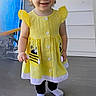 bee_patch, black_leggings, casual, child, clothing, cute, hair, happy, outside, person, pigtails, porch, small_child, smiling, socks, standing, toddler, wooden_floor, yellow_dress, young_child