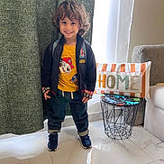 Moussa participe au concours pour gagner de l'argent avec cette photo : child, smiling, indoor, curly_hair, yellow_tshirt, jacket, jeans, sneakers, backpack, pillow, home_decor, table, window, curtain, floor, marble_floor, living_room, person, cute, happy