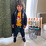 child, smiling, indoor, curly_hair, yellow_tshirt, jacket, jeans, sneakers, backpack, pillow, home_decor, table, window, curtain, floor, marble_floor, living_room, person, cute, happy