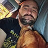 Mona is registered to the contest to win money with this photo: man, dog, beard, bald, cuddling, lying_down, pillow, indoor, close_up, pet, comfort, resting, casual, shirt, facial_hair, head, face, brown_dog, human, relaxation