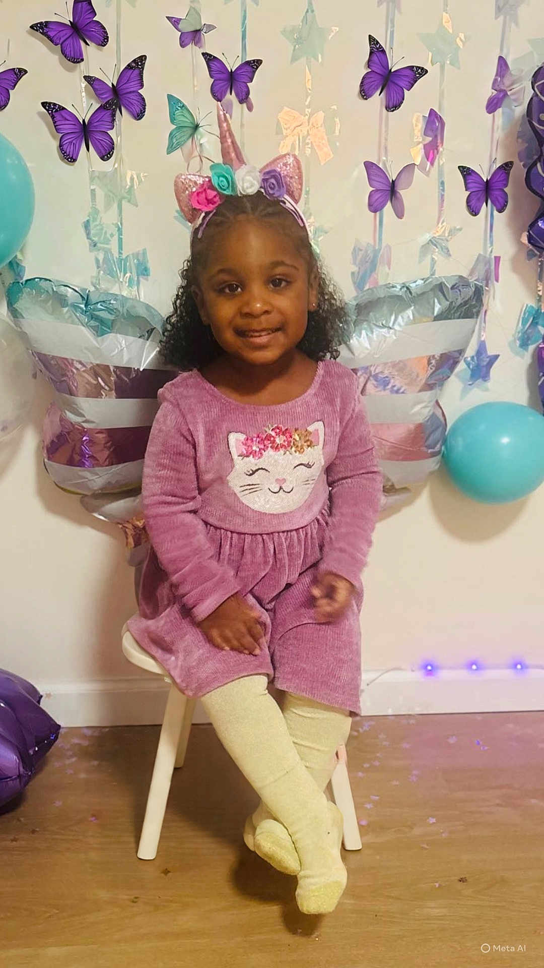 Xianah is registered to the contest to win money with this photo: child, girl, purple_dress, unicorn_headband, butterfly_decorations, balloons, smiling, indoor, party, chair, curly_hair, tights, floor, wall_decor, festive, cute, happy, portrait, sitting, celebration