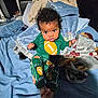 baby, bed, blanket, blue_bedding, child, cozy, curly_hair, cute, football_clothing, green_outfit, indoors, infant, looking_at_camera, pajamas, portrait, resting, sleepwear, soft_toys, toddler, young_child