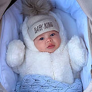 King joined the competition — help win amazing prizes! baby, infant, hat, pom_pom, winter_clothing, blanket, stroller, blue, white, cute, face, child, warm, soft_texture, portrait, clothing, outdoor_gear, newborn, cozy, sleeping_bag