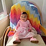 baby, child, girl, pink_dress, boots, chair, knitted_blanket, rainbow_colors, window_light, indoors, smiling, happy, cute, portrait, seated, wooden_armrest, toddler, hair_clip, fabric, cozy