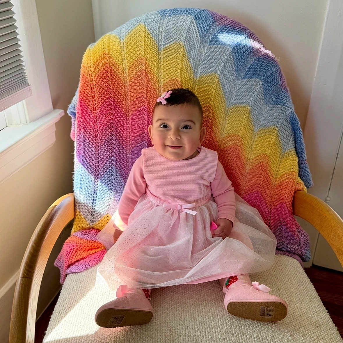 Kimiya joined the competition — help win amazing prizes! baby, child, girl, pink_dress, boots, chair, knitted_blanket, rainbow_colors, window_light, indoors, smiling, happy, cute, portrait, seated, wooden_armrest, toddler, hair_clip, fabric, cozy