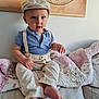 toddler, child, boy, blue_polo, beige_pants, suspenders, striped_cap, couch, quilt, floral_pattern, indoor, portrait, cute, curious, seated, vintage_map, wall_art, barefoot, light, home