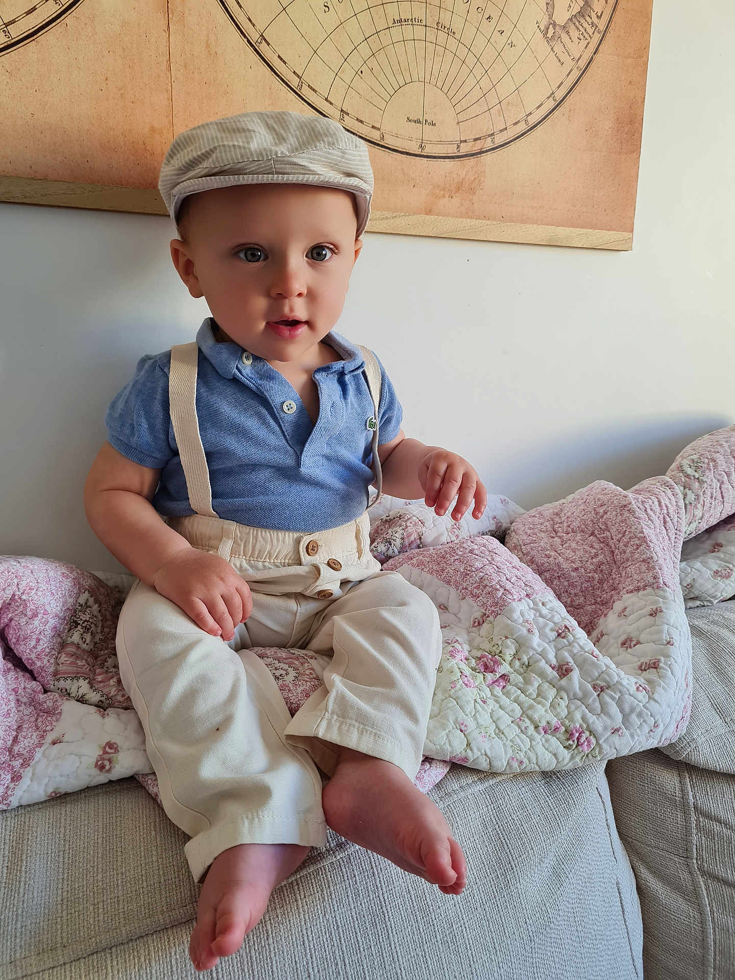 Sacha participe au concours pour gagner de l'argent avec cette photo : toddler, child, boy, blue_polo, beige_pants, suspenders, striped_cap, couch, quilt, floral_pattern, indoor, portrait, cute, curious, seated, vintage_map, wall_art, barefoot, light, home