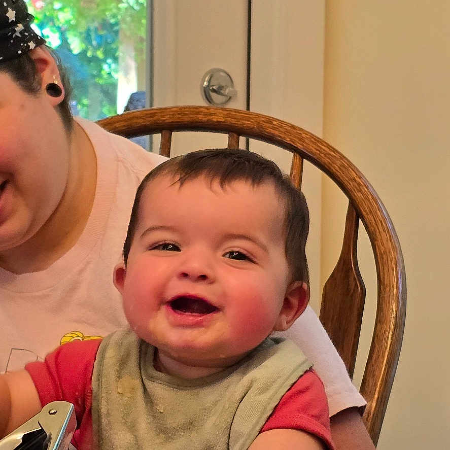 Beck is registered to the contest to win money with this photo: adult, baby, casual, chair, child, clothing, curtains, family, floral_pattern, happy, headband, home, indoor, love, person, portrait, smile, table, toddler, wooden_chair