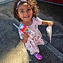 child, girl, curly_hair, headband, milk_carton, dress, minnie_mouse, pink, shoes, outdoor, sunlight, pavement, car, red_car, smile, happy, person, holding, paper_bag, cute
