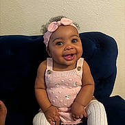 Jaisley is registered to the contest to win money with this photo: baby, child, smiling, pink_headband, knitted_dress, white_tights, sitting, couch, blue_couch, indoor, portrait, happy, cute, person, infant, headband, wall, furniture, skin, face
