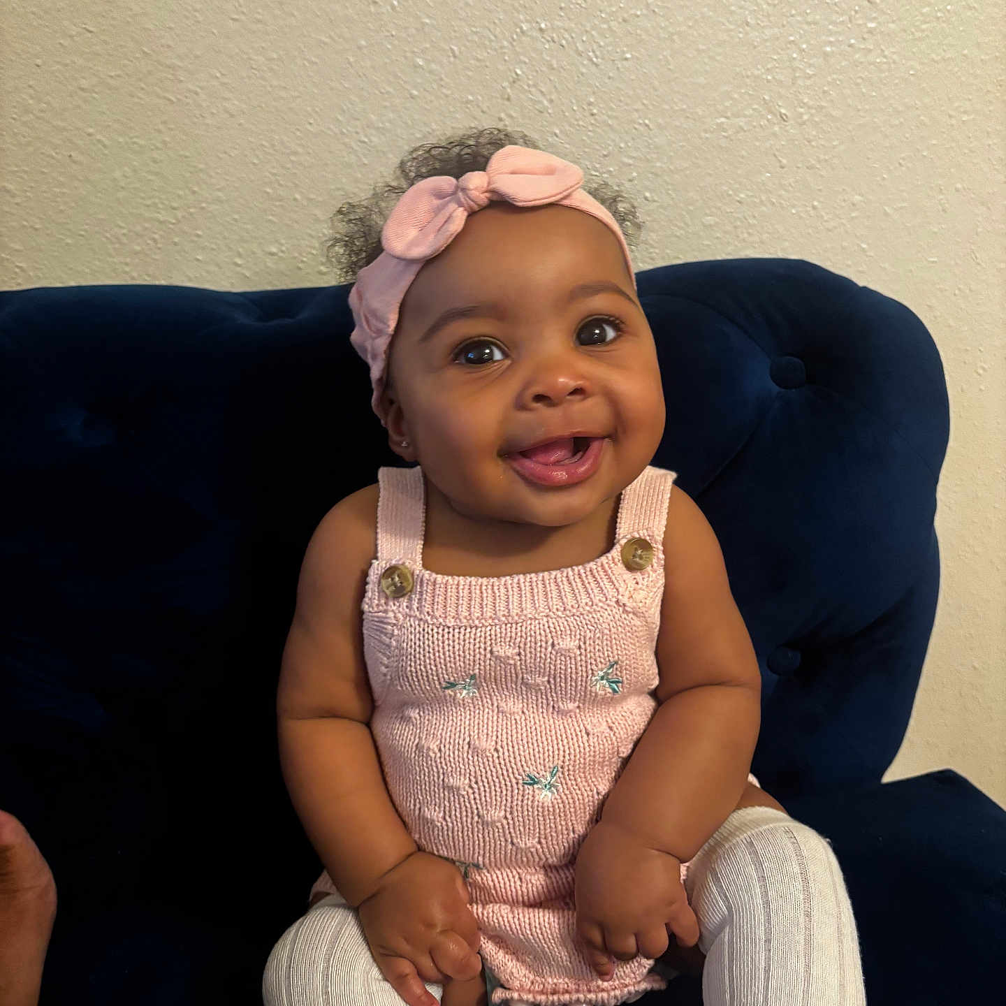 Jaisley is registered to the contest to win money with this photo: baby, child, smiling, pink_headband, knitted_dress, white_tights, sitting, couch, blue_couch, indoor, portrait, happy, cute, person, infant, headband, wall, furniture, skin, face