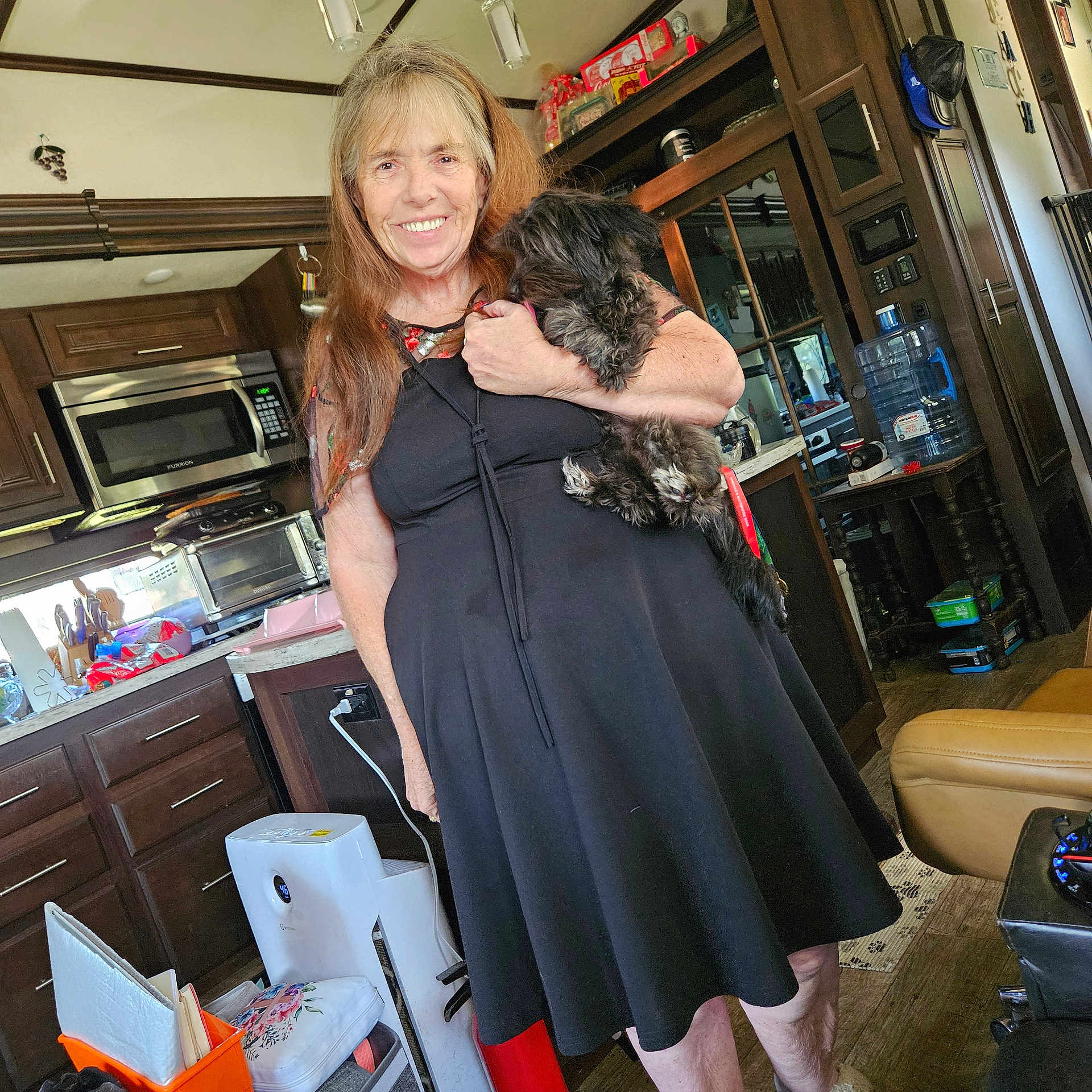 Brenda Copenhaver is registered to the contest to win money with this photo: appliances, black_dress, casual, chair, countertop, dog, floor, happy, holding, home, indoor, kitchen, long_hair, person, pet, smile, table, water_dispenser, woman, wooden_cabinets